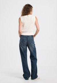 Cream sleeveless knit top with a ribbed texture, paired with loose denim jeans featuring back pockets and a relaxed fit.