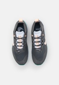 Chaussures de sport grises avec dessus en mesh, lacets noirs, accents roses et semelle grise texturée, arborant un logo blanc sur le côté.