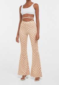 Brązowe i białe krateczkowe spodnie dzwony z wysokim stanem, połączone z dopasowanym białym crop topem. Materiał jest gładki z lekkim połyskiem.