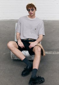 White and tan striped short-sleeve shirt with a chest pocket, black shorts, gray socks, and black shoes, sitting on a textured gray surface.
