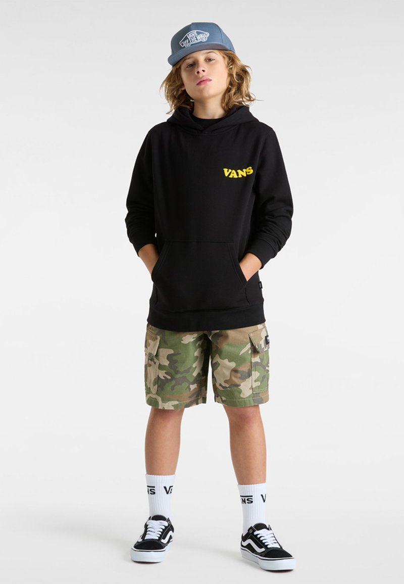 Felpa nera con cappuccio e logo giallo "VANS", pantaloni cargo mimetici, sneakers nere, calzini bianchi con testo "VANS", cappellino blu.