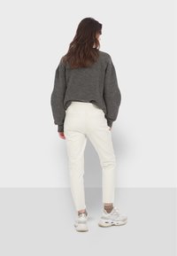 Szara krótka sweter, białe dopasowane spodnie i buty sportowe. Miękka tekstura, luźny krój, elastyczny pas i widoczne detale szwów.