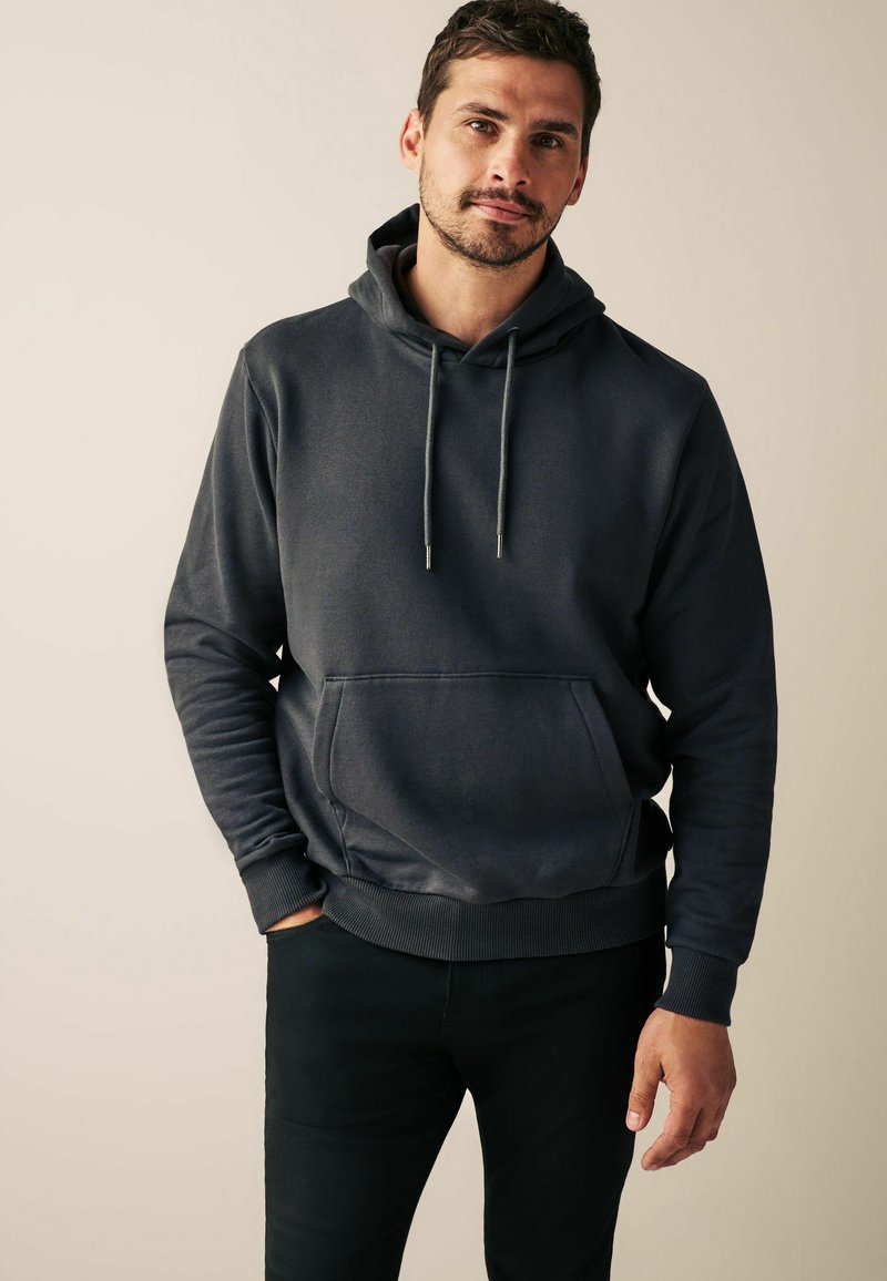 Haut à capuche gris foncé avec une poche avant, cordon de serrage réglable, poignets et ourlet côtelés. Design ajusté avec une texture lisse.