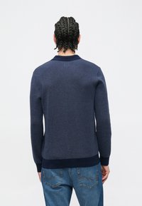 Marineblauer Pullover mit einer strukturierten Stoffstruktur, gerippten Bündchen und Saum. Verfügt über ein Kragensdesign und wird mit hellblauen Jeans getragen.