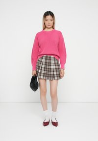 Sweater riscado em rosa brilhante combinado com uma saia xadrez castanha. Bolsa preta, meias brancas e mocassins vermelhos completam o look.