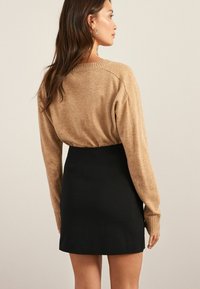 Beige neule pitkähihaisilla ja ribatulla hihalla, yhdistetty tiukkaan mustaan minihameeseen. Silkkiset tekstuurit, minimalistinen muotoilu.