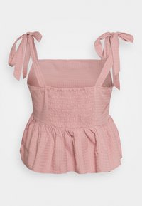Top peplum rosa com tecido texturizado, alças ajustáveis com laço e cintura franzida, apresentando um design fluido e um padrão de diamante subtil.