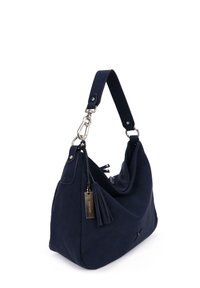 Marineblaue Handtasche mit breitem Schultergurt, silbernen Metallverschlüssen, einem Quastenanhänger und einem rechteckigen Metallmarkenschild, das an der Seite hängt.