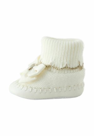 White bootie made of soft knitted material with ribbed texture. Features decorative bow and metallic chain accent around the ankle.