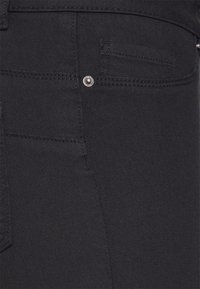 Pantalones vaqueros de mezclilla negra con una textura suave, que presentan un bolsillo sutil y un detalle de botón de metal cerca de la cintura.