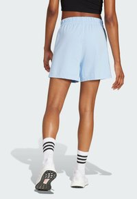 Shorts en coton bleu clair avec une taille élastique, offrant une coupe décontractée. Associés à des baskets blanches et des chaussettes à rayures noires.