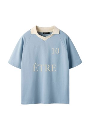Lyseblå kortærmet skjorte med cremet krave, "10" trykt øverst til højre og "ÊTRE" centreret foran i cremefarvet skrift.