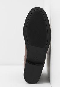 Semelle d'une chaussure en cuir marron avec une semelle extérieure en caoutchouc noir, taille 37, montrant un motif de grip texturé et un détail du talon sur fond blanc.