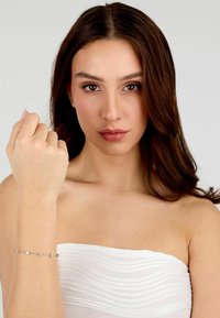 Bracciale in argento con piccole gemme rettangolari e rotonde, indossato su un polso, con un design a catena liscia.