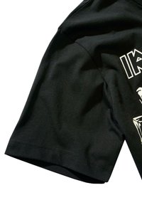 Juodas medvilninis marškinėliai su trumpomis rankovėmis, lygiu paviršiumi ir baltu piešiniu priekyje. Matomi subtilūs siuvimo detalės.