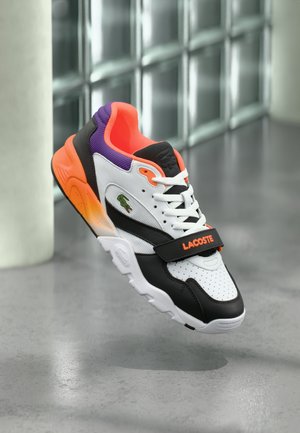 Sneakers Lacoste con design bianco, nero e arancione e tacco viola. Presentano dettagli traforati e una chiusura in velcro.