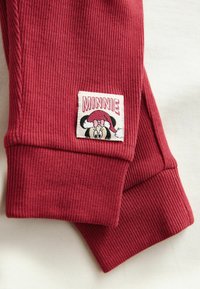 Piros bordás leggings, fehér folttal, amelyen egy hímezett Minnie Mouse látható, valamint a "MINNIE" név rózsaszín betűkkel.