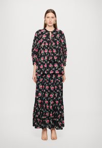 Svart blomstermønstrete antrekk med en luftig bluse med puffede ermer og et matchende lagdelt skjørt, begge prydet med rosa roser.