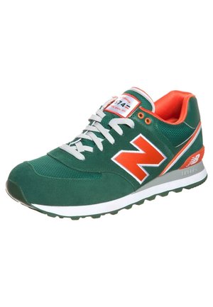 Zielono-pomarańczowy but New Balance z białymi sznurówkami, pomarańczowym logo "N" i białą środkową podeszwą z fakturowaną podeszwą.