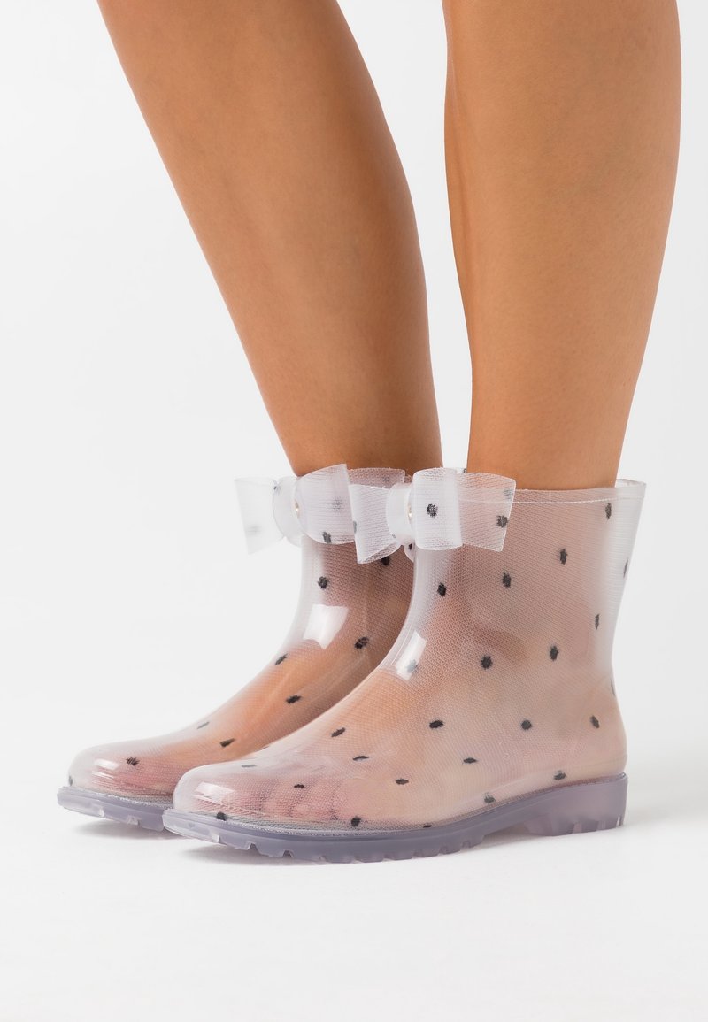 Clear, polka-dotted rain boots with a translucent design, featuring a bow accent at the ankle and a textured rubber sole.