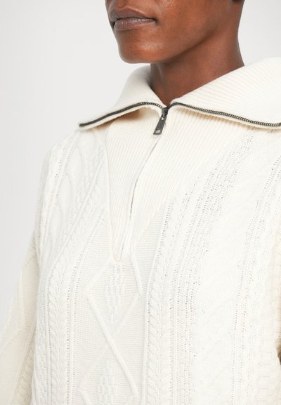 Suéter de punto color crema con un alto cuello, media cremallera y patrones de cable texturizados. Tela suave con detallado intricado.
