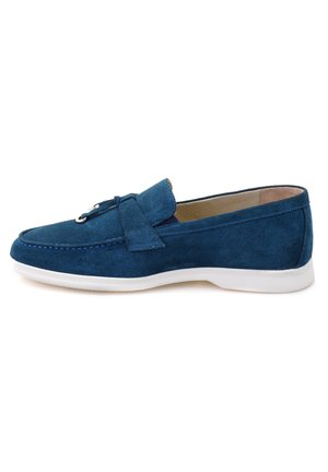Blauwe suède instapper met een zachte textuur, witte rubberen zool, een decoratieve strikaccent aan de voorkant en gedetailleerde stiksels langs de randen.