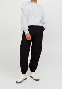 Ljusgrå tröja med rund hals, svarta cargobyxor med fickor och vita sneakers med grå sulor. Avslappnad outfit med bekväm passform.