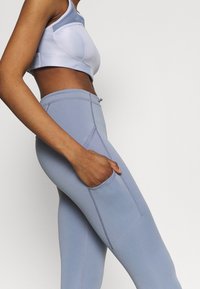 Soutien-gorge de sport bleu clair avec des accents en maille, associé à un legging taille haute assorti avec une poche latérale et des coutures visibles.