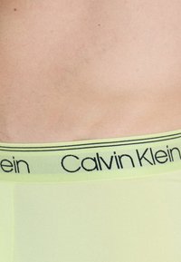 Calvin Klein neonsko rumeno spodnje perilo z črnim logotipom na pasu. Gladka tekstura in prilegajoča zasnova, ki jasno prikazuje blagovno znamko.