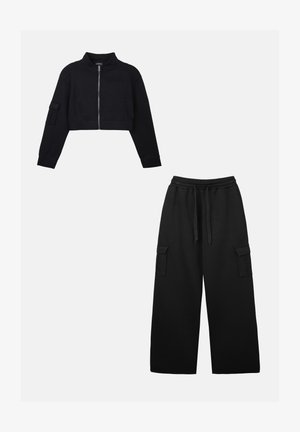 Fekete, rövidített cipzáros dzseki hosszú ujjakkal és oldalsó zsebekkel, széles szárú fekete melegítőnadrággal, ami cargo zsebekkel rendelkezik.