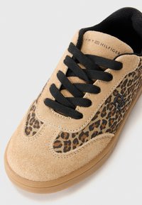 Baskets en suède beige avec des lacets noirs, des panneaux en imprimé léopard, une semelle en gomme et le logo Tommy Hilfiger sur le côté et la languette.