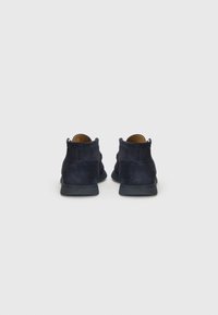 Bocanci ankle din suede de culoare albastru închis, cu o textură fină, având vârful rotund și tălpi flexibile din cauciuc, prezentați din perspectiva din spate.