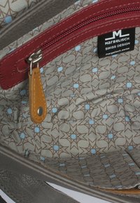 Inuti en grå läderhandväska finns ett röd dragkedjefack. Fodrad med ett mönstrat tyg i beige, brunt och ljusblå stjärnmotiv.