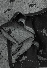 Szary koc z miękkiego materiału, charakteryzujący się teksturowanym, tkanym wzorem i kontrastującymi ciemniejszymi plamami. Krawędzie są przeszyte ciemniejszą nicią.