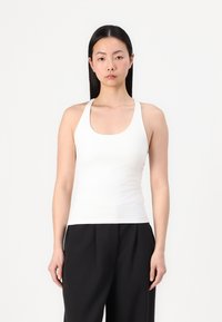 Witte tanktop met een ronde hals en brede schouderbanden, aansluitend ontwerp, zachte textuur, gecombineerd met losse zwarte broeken.