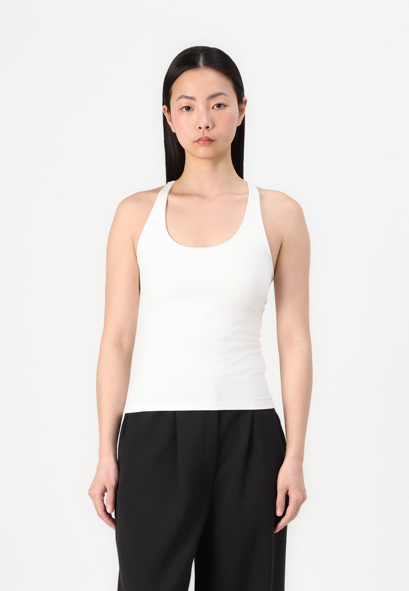 Witte tanktop met een ronde hals en brede schouderbanden, aansluitend ontwerp, zachte textuur, gecombineerd met losse zwarte broeken.