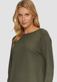 Ciemnozielony długi rękaw top wykonany z miękkiego materiału z okrągłym dekoltem i subtelnymi szwami, o luźnym kroju i bez widocznych wzorów.