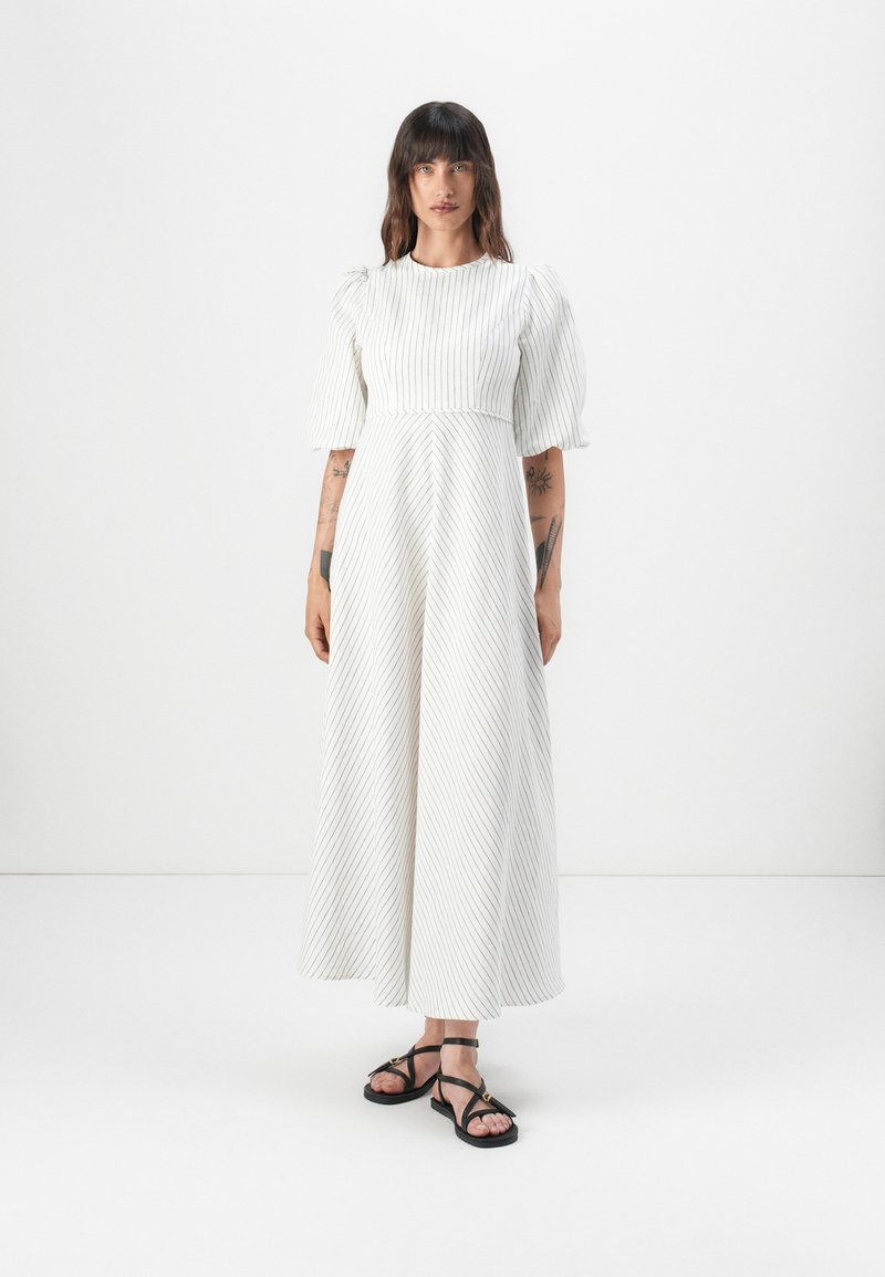 Hvidstribet maxikjole med korte pufferm, en tætsiddende bodice og en bred nederdel; parret med sorte strop sandaler.