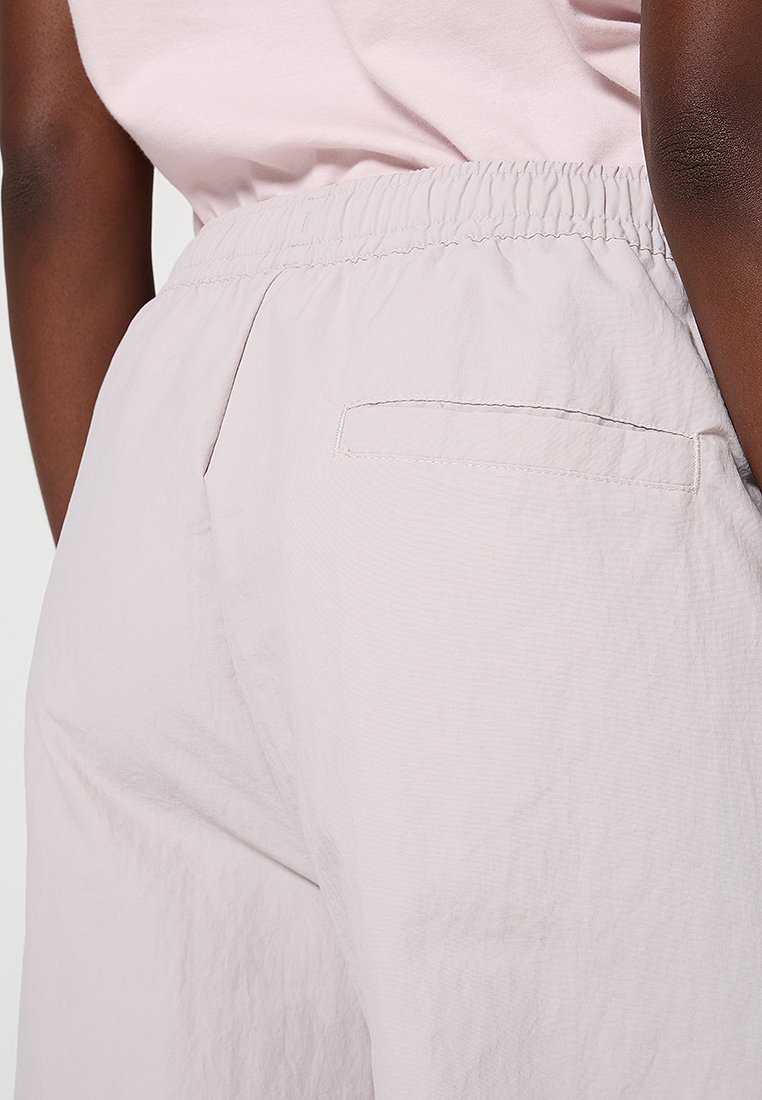 Pantalons légers de couleur rose clair, avec une taille élastique, comprenant une poche arrière et un fini en tissu texturé.