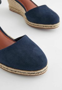 Sandali wedge in suede blu navy con punta rotonda, tacco avvolto in juta e dettagli in pelle marrone all'interno. Superficie testurizzata per una maggiore aderenza.