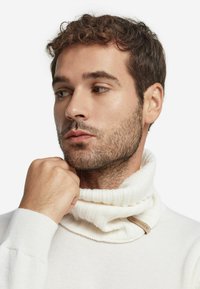 Hvid ribbet turtleneck sweater med en foldet krave, der har et stofmærke ved halsudskæringen. Blød tekstur og tætsiddende design.