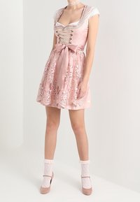 Abito di raso rosa con scollo allacciato, motivi floreali ricamati e un fiocco in vita. Indossato con calze di pizzo bianche e scarpe rosa.
