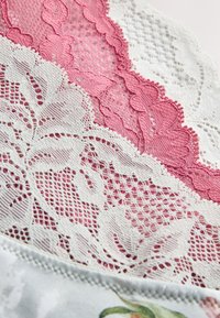Detaljeret close-up af hvid og lyserød blonderstof med blomsterprint og fin mesh-tekstur.