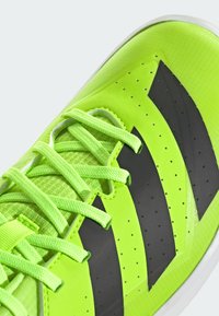 Jasne zelené športové topánky s čiernymi akcentmi, textúrovaný zvršok, perforácie a ploché šnúrky, navrhnuté pre výkon a pohodlie.