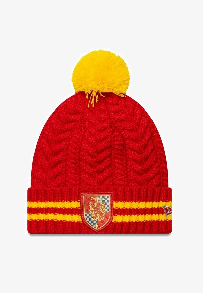 Red knitted beanie with a yellow pom-pom on top, featuring a ribbed band with two horizontal yellow stripes and a crest on the front.