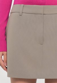 Beige skjørt med en jevn tekstur, med flat front, en enkelt lomme og rett snitt. Kombinert med en rosa ribbestrikket genser.