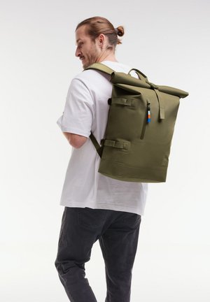 Zaino a rullo verde oliva con spallacci regolabili, zipper frontale e piccolo tag accessorio colorato. Materiale impermeabile, design minimalista.