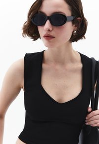 Top negro sin mangas con un escote en V profundo y textura suave. Combinado con gafas de sol ovaladas negras y un bolso negro, con detalles en plata.