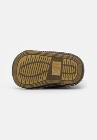 Sola de sapato de borracha preta com padrão texturizado de aderência, bordas reforçadas e detalhes em pesponto amarelo. Apresenta um logótipo da marca na palmilha.