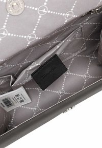 Interior de bolso gris con forro de patrón geométrico, etiqueta de marca de cuero negro y un pequeño bolsillo de almacenamiento. Herrajes plateados visibles.